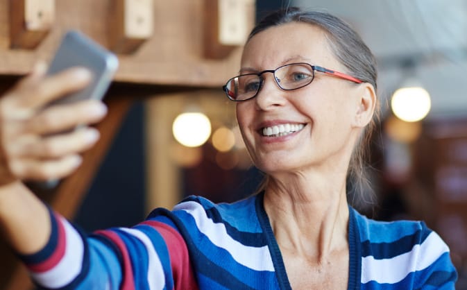 middle-aged woman wearing glasses smiling while holding out her phone, taking a selfie