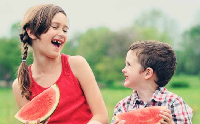 two children eating watermelon. the little girl has a missing tooth